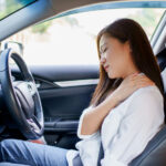 Young woman gripping her shoulder in pain after a car accident engaged her seat belt and locked into place