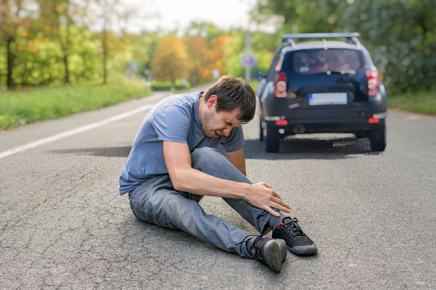 Man holding ankle in pain after being hit by a car while walking in the road