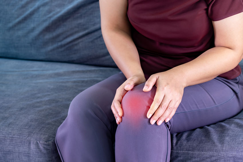 Older woman sitting on couch at home while experiencing knee pain caused by an osteoarthritis flare up