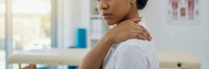 A woman experiencing shoulder and upper back pain in a physical therapy clinic setting.